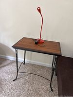 Side table with wood top and wrought iron legs, red desk lamp on top.
