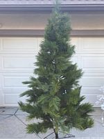 Front views of the 7.5-foot tall artificial Christmas tree with green needles and some lights attached, standing in front of a white garage door.