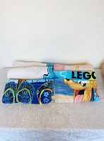 Folded Legoland beach towels showing colorful character graphics including blue sandals and part of a face