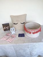 View showing beige eyelash throw pillow, white ceramic hand cell phone holder, 11 rings on blue card, pink socks, Harry Styles CD, fiber basket with orange tassels