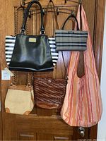 Overall view of five handbags hanging on door hooks, showing different styles and materials