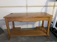 Front angled view of oak wood computer desk showing shape, leg design and lower shelf.