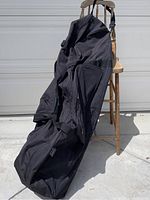 Black rolling travel golf bag hanging on a chair outdoors, showing full length and compartments.