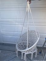 White childrens rope swing chair hanging on a hook, showing circular rope net seat, hanging ropes, and fringed tassels.