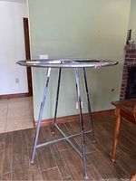 Full view of round collapsible clothing rack with four vertical chrome legs and round top ring. Some wear and pink string tied on one leg visible.