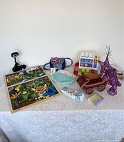 Full view of lot items on white cloth including puzzles, toy cash register, crocheted purses, wagon, chalk, ornaments
