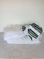 White folded bedding including covers and pillow shams with some striped pillow shams visible