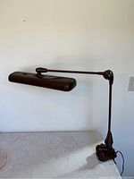 Side view showing the articulating arm extended with the lamp housing horizontal and clamp base on table edge.