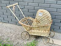 Full side view of the antique wicker doll's pram showing the curved woven wicker hood and handlebar detail with ribbon.