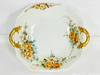 Porcelain bowl with two ornate gold-painted handles and hand-painted yellow rose floral designs with greenery