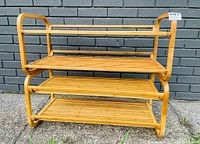 Photo showing larger bamboo 2-tier shoe shelf with curved side rails and slatted shelves, outdoors against gray brick wall