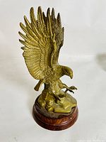 Brass eagle sculpture with detailed wings spread wide visible from the side, mounted on a wooden base, photographed on a white background.