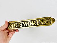 Side angle photo showing thickness and raised lettering of the solid brass 'NO SMOKING' wall plaque.