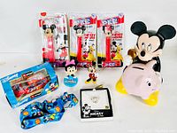Photo showing the entire Disney Mickey Mouse collectible lot including PEZ dispensers, piggy bank, figurines, car collectible, pendant, lanyard, and keychains.