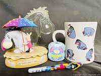 Front view of collection showing Eeyore and Piglet figurine with umbrella, Eeyore mug, shower mitt, and pen laid out together.