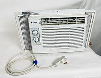 Full view of GREE white window air conditioner showing front control dials, vent grill, adjustable side panels, and attached power cord with plug.