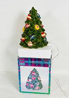 Porcelain ceramic Christmas tree atop its original box showing front view, lighted tree image on box.