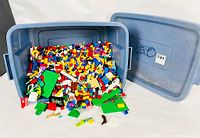 Bin containing assorted colorful Lego bricks, green baseplates, and parts.
