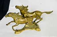 Front side view of brass galloping horses figurine on white background, showing two horses with detailed manes and muscular forms.