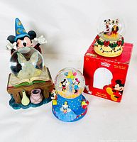 Photo showing all three Disney snow globes including the Sorcerer's Apprentice Mickey, the Christmas Mickey & Pluto with original box, and the 100th Birthday musical globe with multiple character figures.