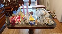 Table top covered with various pressed glass candle holders, hurricane covers, bowls, platters, and ceramic items