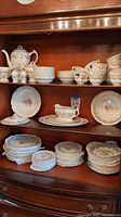 Full view of china set on shelves including teapot, cups, bowls, plates in floral and gold leaf design