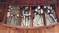 Top view of drawer filled with assorted flatware including spoons, forks, and knives in multiple styles and finishes.