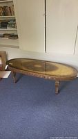 Side view of the oval coffee table showing carved legs and pattern on top surface