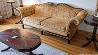 Front angled view of sofa showing floral upholstery, tufted arm, and gilded carved wooden frame with two seat cushions.