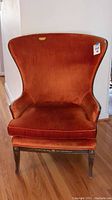 Front view of the orange crushed velour wingback chair showing high curved back and seat cushion.