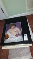 Stack of loose paintings on black portfolio board, top image of a male nude draped in white holding grapes and a jug