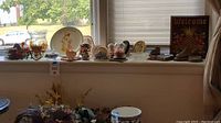 Full view of decorative items on windowsill including plates, plaques, vase, coasters, and bronzed baby shoes.