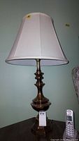 Full view of vintage brass lamp with white shade on a dark wood table against a light blue wall.