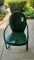 Front view of green metal patio rocking chair showing contoured seat and rounded backrest with vertical ridges.