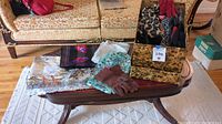 Photo of vintage scarves, brown gloves, leopard print and solid colored fanny packs on a wooden coffee table in living room setting