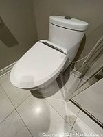 Full view of the white one-piece toilet installed in bathroom, showing the closed bidet toilet seat with power cable connected.