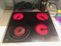Front view of the AEG Electrolux glass electric cooking top with four radiant heating zones glowing red, showing some wear on the glass surface.
