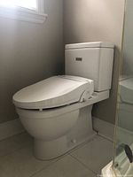 White Duravit two-piece toilet installed in bathroom corner with bidet bidet seat attachment but no seat.