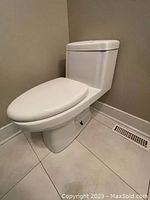 Side view of white one-piece Glacier Bay toilet showing elongated bowl and seat, floor vent nearby.