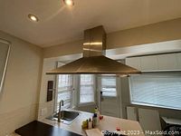 Wide angle view of vent hood installed above kitchen counter with sink and windows in background.