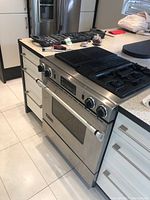 Jenn Air stainless steel gas stove installed in kitchen with four burners and BBQ grates on top.