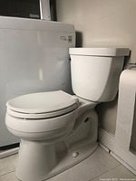 Photo showing side view of the white Kohler toilet installed near a washing machine, seat closed.