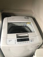 Front and top view of white LG top-loading washing machine with open clear lid and control panel