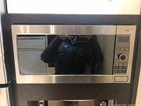 Front of stainless steel Panasonic microwave installed in kitchen with reflective glass door.