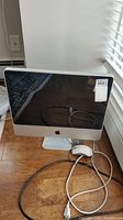 Front view of Apple iMac with 20-inch screen and wired mouse on floor.