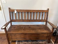 Front view of wooden bench with backrest and armrests showing the hinged seat closed.