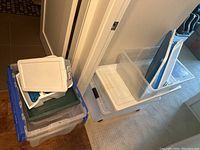 Stack of plastic storage bins of various sizes with lids on a floor near a doorway