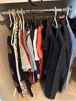 Photo of a closet rod holding multiple clothing items of various colors and types including tops, sweaters, and jackets, showcasing the variety of items in the lot.