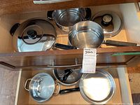 Overview of cookware inside drawer showing Lagostina pot with glass lid, steamer insert, 11-inch frypan with lid, Berlin Kuche pot with lid and other cookware.