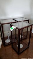Three wood framed display cabinets with clear plastic panels and white doll stands inside. Cabinets are rectangular with dark wood stain and glass-like panels for display.